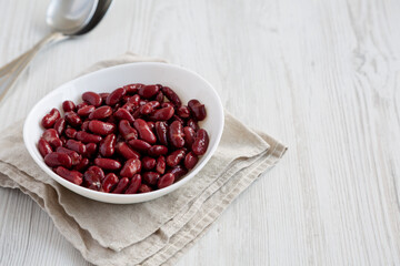 Red Organic Kidney Beans in a White Bowl on a white wooden background, side view. Space for text.