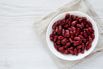Red Organic Kidney Beans in a White Bowl on a white wooden surface, top view. Flat lay, overhead, from above. Copy space.