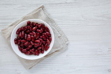 Red Organic Kidney Beans in a White Bowl on a white wooden surface, top view. Flat lay, overhead, from above. Copy space.