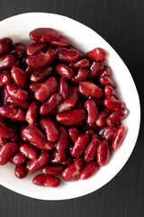 Red Organic Kidney Beans in a White Bowl on a black background, top view. Flat lay, overhead, from above.