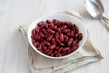 Red Organic Kidney Beans in a White Bowl on a white wooden background, side view.