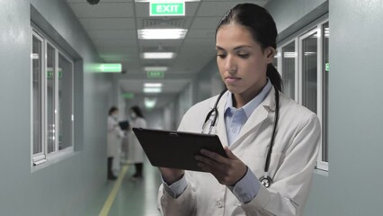 female latin doctor standing in hospital hallway using tablet,hispanic woman medic holding touch screen device in clinic ward checking patient data