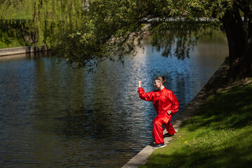 Asian woman in red kimano practicing taijiquan outdoors, chinese martial arts, healthy lifestyle concept.