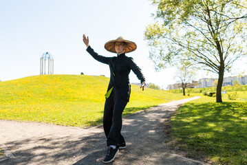 Asian woman with hat practicing taijiquan outdoors, chinese martial arts, healthy lifestyle concept.
