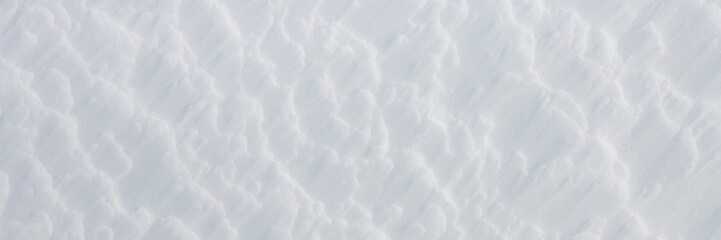 Beautiful winter background with snowy ground. Natural snow texture. Wind sculpted patterns on snow surface. Wide panoramic texture for background and design.