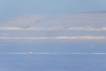 Winter Arctic landscape. Off-road car is driving on snow and ice. Winter ice road along the frozen river. Travel and car trips in the Arctic. Anadyr estuary, Chukotka, Siberia, Far North of Russia.