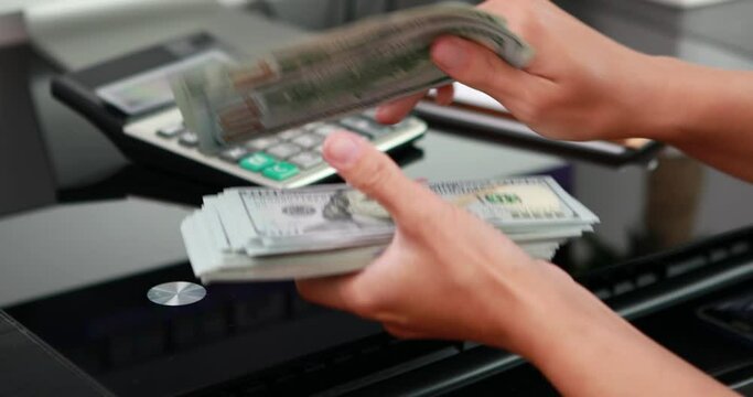 close-up of woman hands counting a stack of hundred-dollar US banknotes.