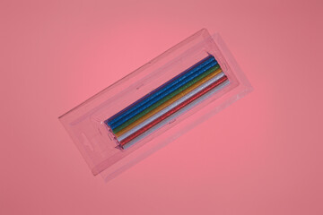 colored shiny sticks of glue for a hot gun in a package on a pink background