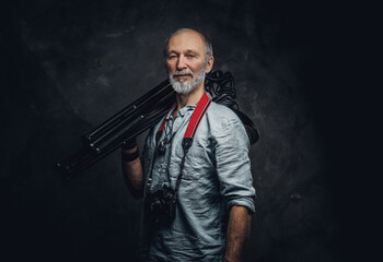 Shot of stylish elderly man photographer with photocamera holding spotlights on his shoulder.