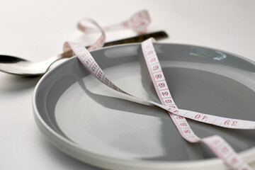 a plate on a light background rewound with a measuring tape and a spoon with a number of diet...