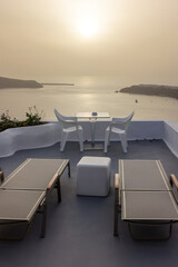 Sun loungers and chairs on terrace in the village of Imerovigli with amazing view of sunset over caldera in Santorini, Greece