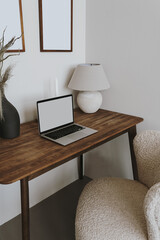 Laptop computer with blank screen on table with lamp and flowers bouquet. Aesthetic influencer boho...
