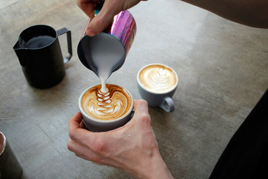 Barista's hand pouring milk into a coffee