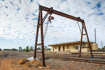 A rusting metal winch framework over railway tracks at a small outback railway station