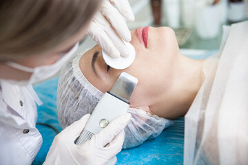 A cosmetologist in white gloves performs care procedures for a woman using an ultrasonic scapula
