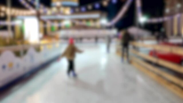 Blurred background. People skating on public open-air ice skating rink in city on winter night. Winter New Year Christmas holidays, decorations illumination garlands flashlights. Activities recreation