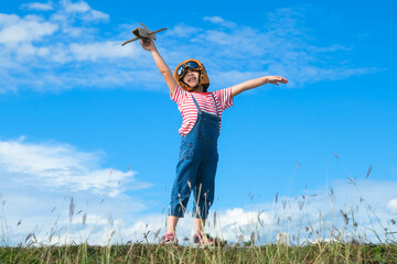 Cute little girl running through the meadow on a sunny day with a toy plane in hand. Happy kid...