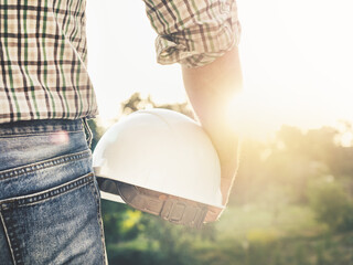 Attractive man in work clothes, holding construction helmet in his hands against the background of...