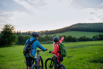 Active senior couple riding electric bicycles on trail at summer park, healthy lifestyle concept....
