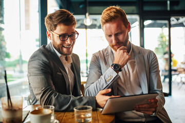 Happy young business people drinking coffee and working with tablet at cafe.