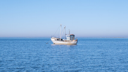 Obraz premium Small white fishing boat floating in the Baltic sea - fisherman out to sea to support his family.