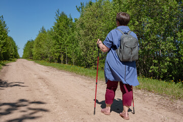 An elderly woman is engaged in Nordic walking.