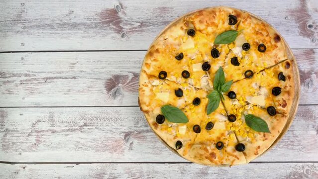 Homemade pizza with cheese, chicken meat, olives and basil leaves rotate slowly.