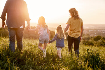 Rear view of family with two daughters walking at the meadow