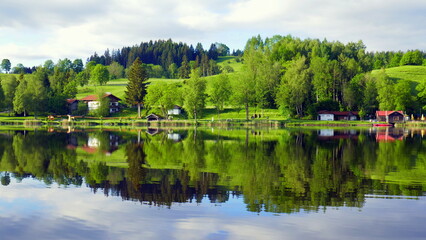 Fototapeta na wymiar Blick über spiegelnden Bad Soier See mit grüner Landschaft und weißen Wolken bei blauem Himmel