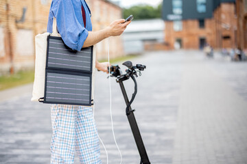 Guy drives electric scooter and charges phone with solar panel on the move. Cropped view. Sustainable business lifestyle and green energy concept © rh2010