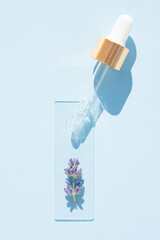 Dropper with transparent cosmetic liquid over blue glass background. Texture of lavender cosmetic essential oil, herbal beaty treatment. Vertical image
