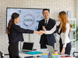 Two happy millennial professional successful businesswomen in formal suit standing shaking hands greeting together when business deal agreement done while businessman entrepreneur smiling clapping