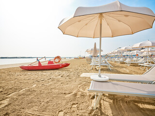 Lifeguard tower next to a lifeboat on the beach on a sunny summer morning, in the background some bathers cooling off on the Adriatic coast, Italy.