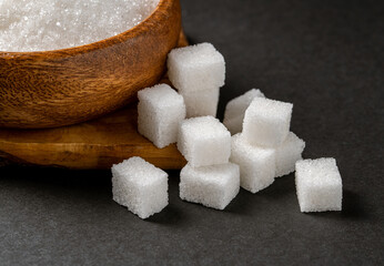 Granulated sugar and sugar cubes in wooden bowl on dark background