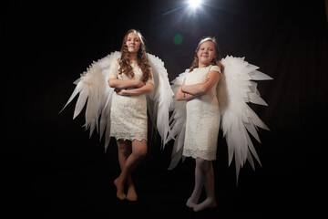 Two teenage girl in white dress and with white wings in a dark studio with bright flash. Sisters...
