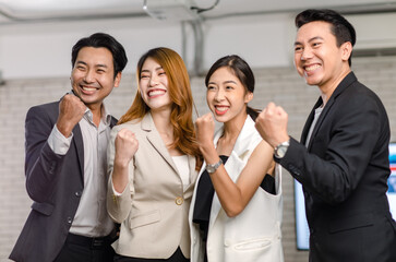 Obraz premium Group of Asian happy cheerful millennial professional successful male businessmen and female businesswomen in formal suit standing holding hands raised fists up celebrating job achievement together