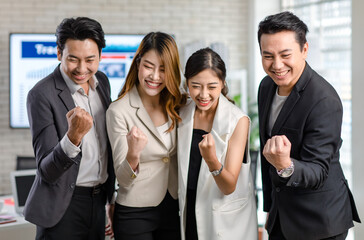 Obraz premium Group of Asian happy cheerful millennial professional successful male businessmen and female businesswomen in formal suit standing holding hands raised fists up celebrating job achievement together