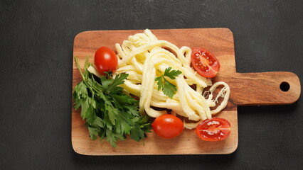 String cheese or cheese whip - salty snack cheese with cherry tomatoes and herbs on chopping board. Turkish cheese