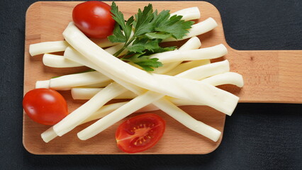String cheese or cheese whip - salty snack cheese with cherry tomatoes and herbs on chopping board....