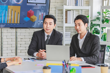 Two Asian professional successful male businessman employee in formal suit sitting together using laptop notebook computer while listening to company customer briefing job description in meeting room