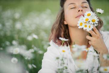 Young beautiful woman enjoying flowers in beautiful chamomile field.