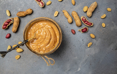 peanut paste in an open jar in spoon near creamy peanut butter peanuts scattered on a dark background, place for text, top view