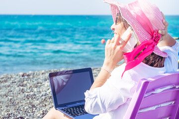 woman smart working on the beach with phone and laptop seen from behind