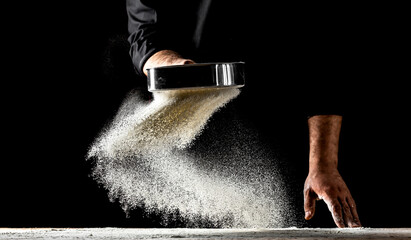 the chef sprinkles flour through a sieve, Powdery flour flying into air. chef hands with flour in a freeze motion of a cloud of flour midair