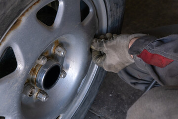 Fototapeta premium Hands of the master in gloves tightening the bolts on the wheel. Changing tires on a car. Car service.