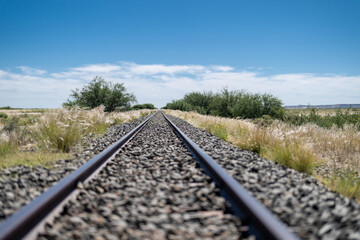 A photo of a kilometer long and straight train track in Namibia. Blue sky with white clouds in...