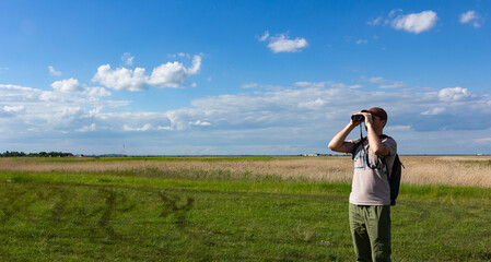 Guy looking at binoculars. Man in t-shirt with backpack. Tourist looking for a way during a trip.