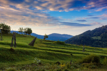 rural landscape in mountains at dawn. field on a hill beneath an autumn sky with glowing clouds....