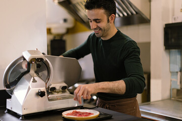 man in the restaurant kitchen preparing slices of carpaccio using the slicer