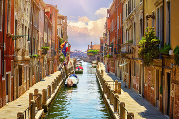 Venice, Italy. Boats, parked near brick walls of houses at street above water of channel. Sunny landscape. Summer day.